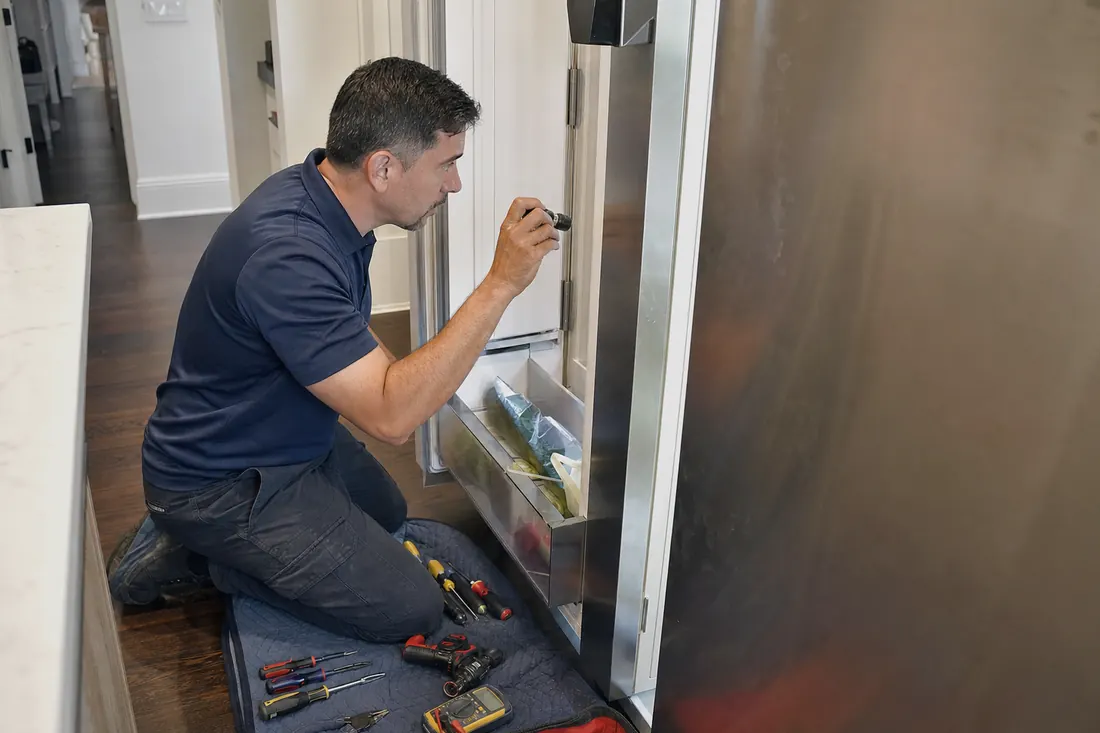 Technician checking inside an open built-in refrigerator with a flashlight, his hand steadying the door in frame - Sub-Zero Ice Maker Not Making Ice